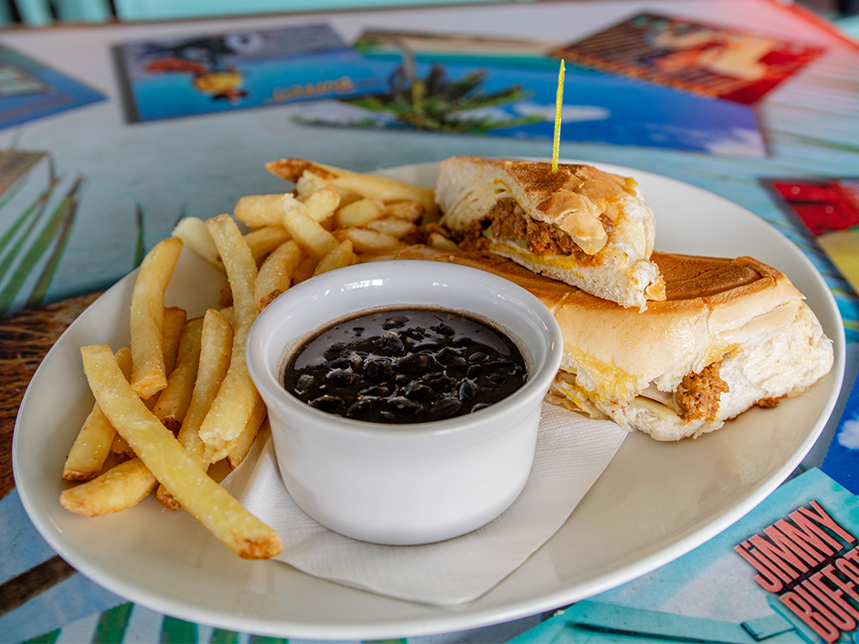 Plate of the Cuban Meatloaf Sandwich with a side of French fries and black beans, a dish on the new menu at Jimmy Buffett's Margaritaville in Universal CityWalk.