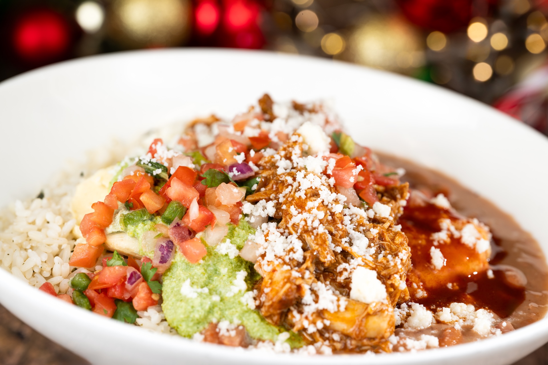 “Christmas-style” Chicken Tamale with mild red chile sauce and pumpkin seed salsa verde, cilantro rice, pinto beans, and queso fresco