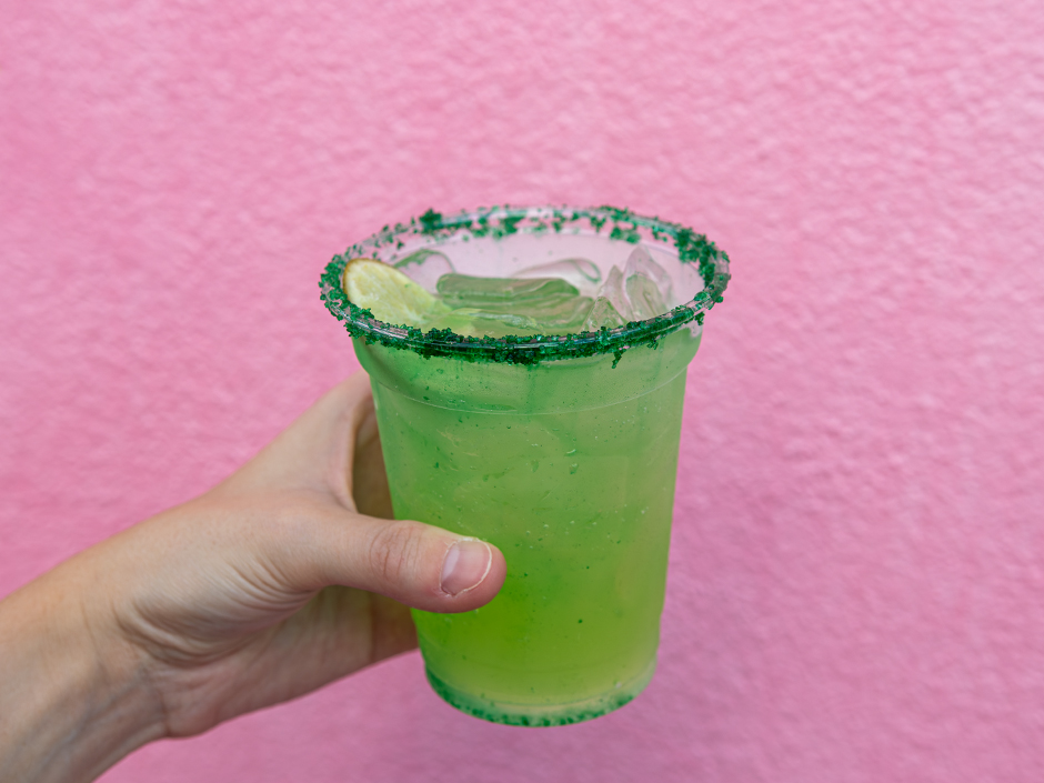 A hand holding a cup of the Enchanting Elixir in front of a pink wall at Universal Studios Florida for
