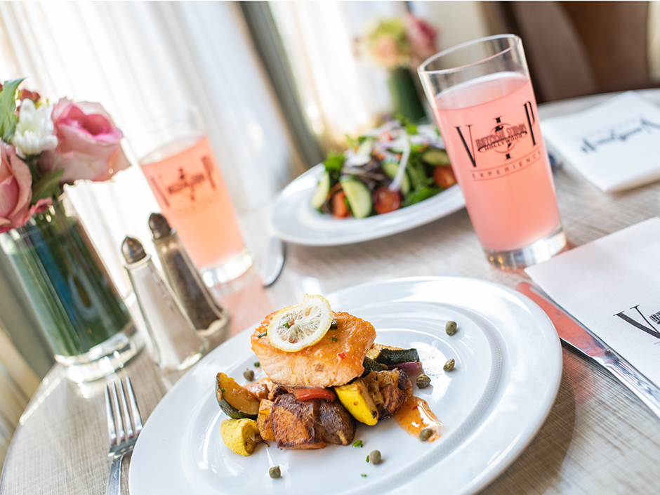 Plate of salmon on roasted veggies and glass of pink lemonade at VIP Dining.