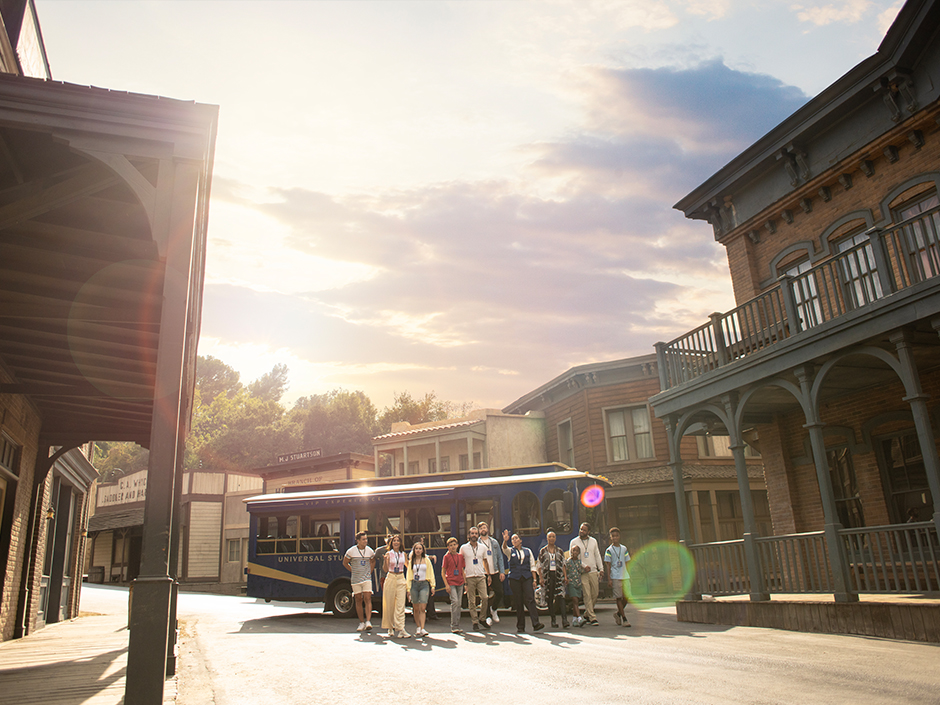 Universal Studios Hollywood VIP tour group and standing in front of blue VIP trolley on Old Western movie set.