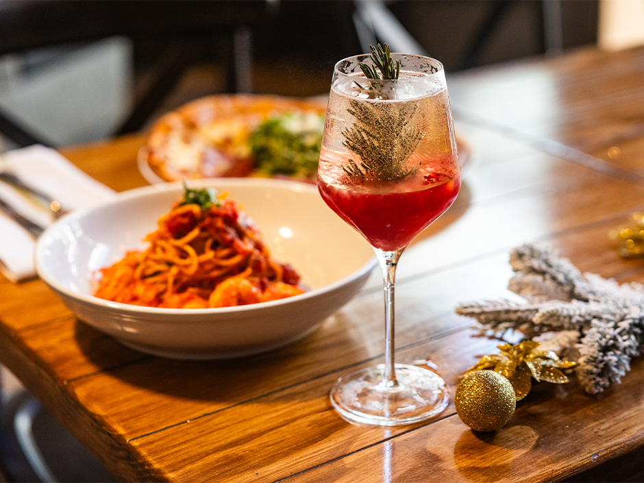 A holiday themed cocktail in a wine glass with cranberry and rosemary.